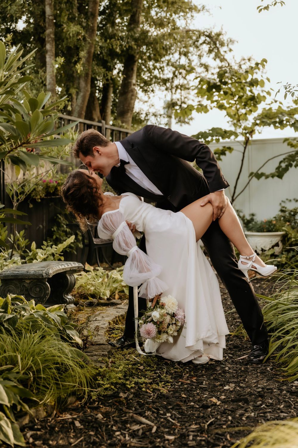 A dramatic dip pose between newlyweds in a garden setting.