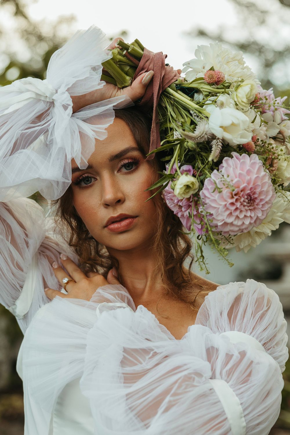 Romantic bridal portrait with flowing white dress and floral crown against natural backdrop.