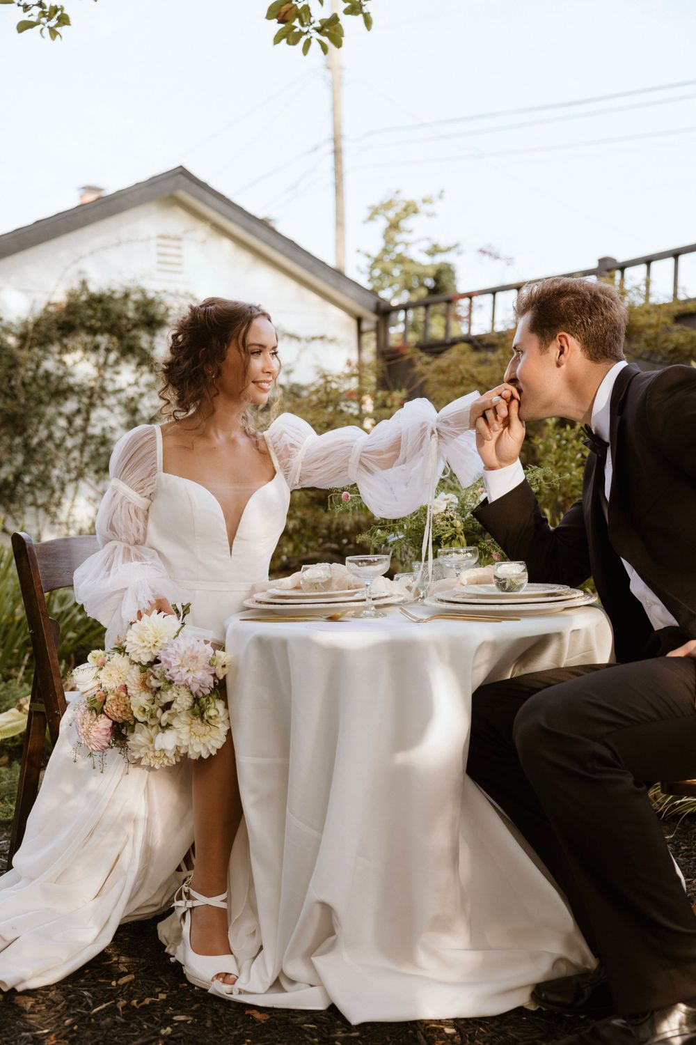 A newlywed couple shares a romantic moment at an outdoor table setting.