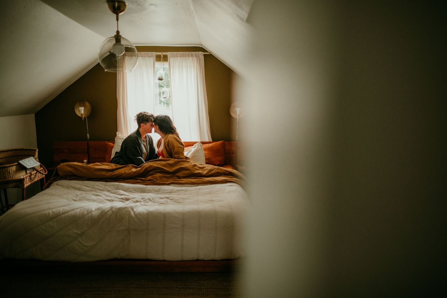 queer couple touches noses together in bed during maternity photography session portland kimberly marie kimble