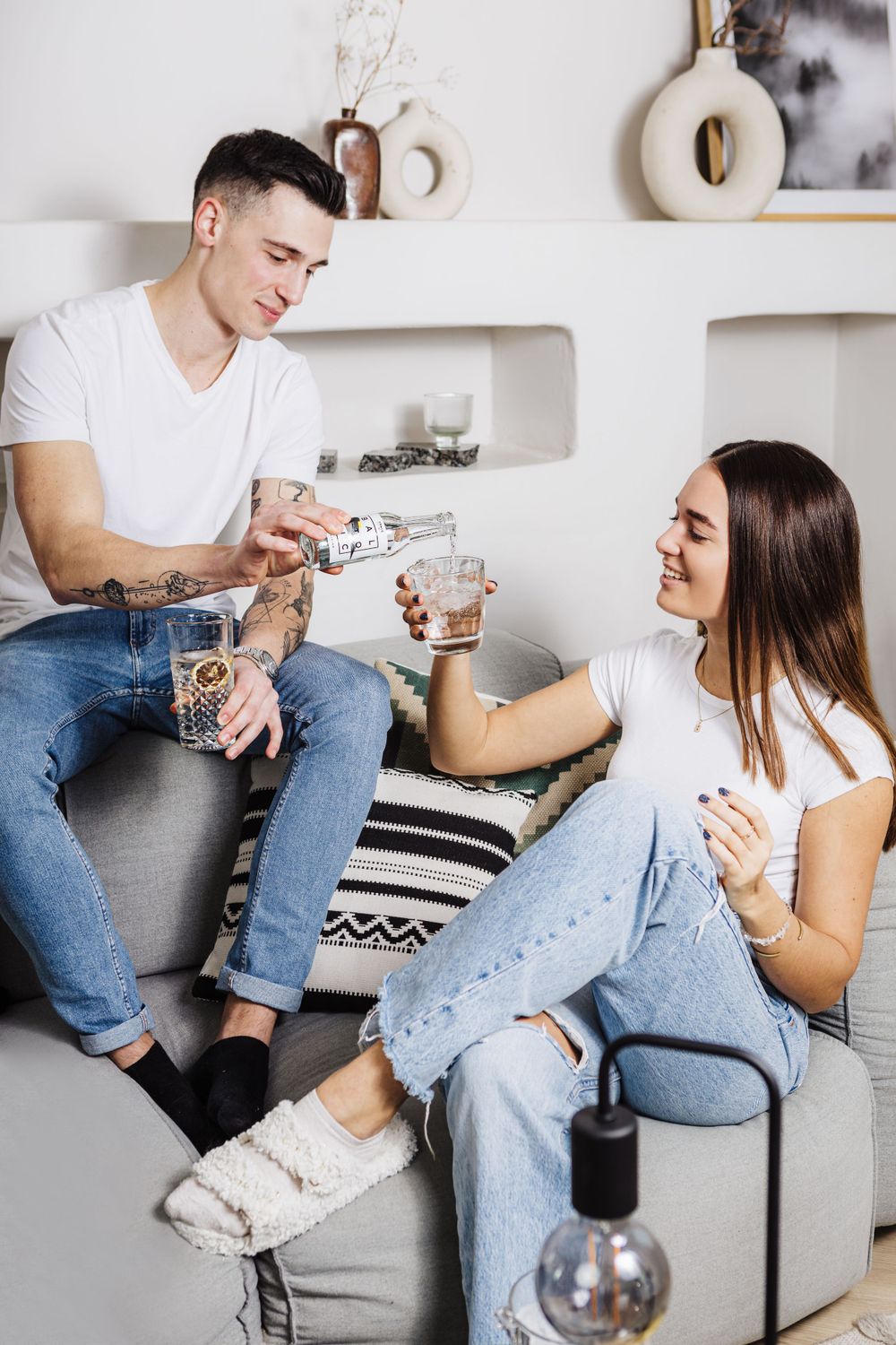 Two people sharing drinks and conversation while relaxing on a comfortable gray sofa.