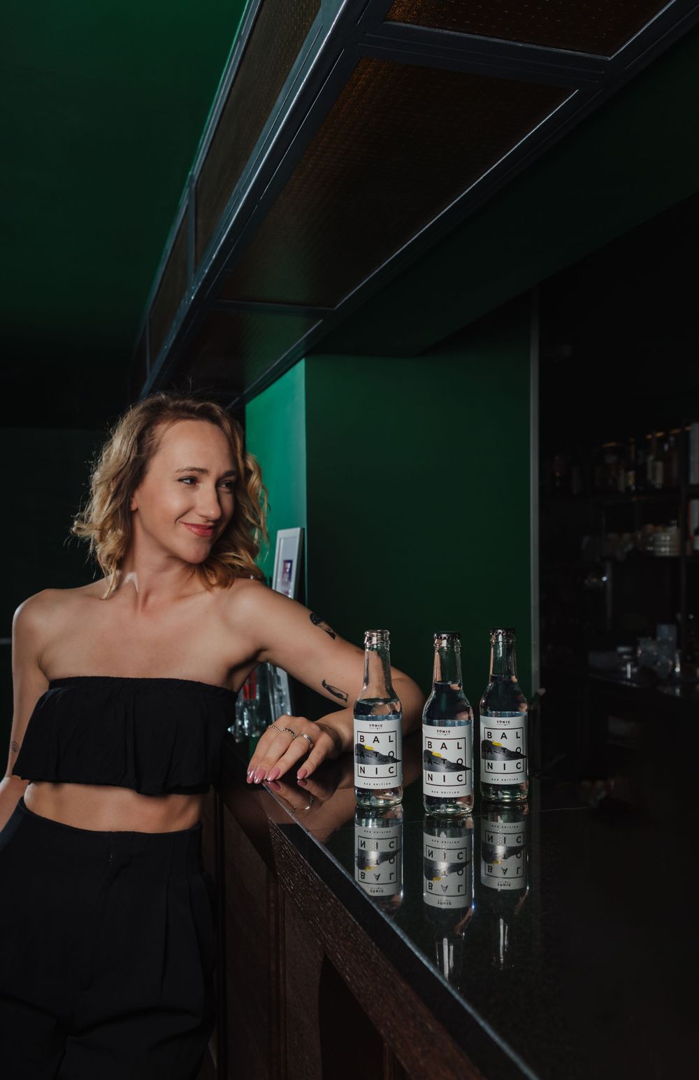 Person arranging bottles of alcohol on a dark wooden shelf in a dimly lit bar.