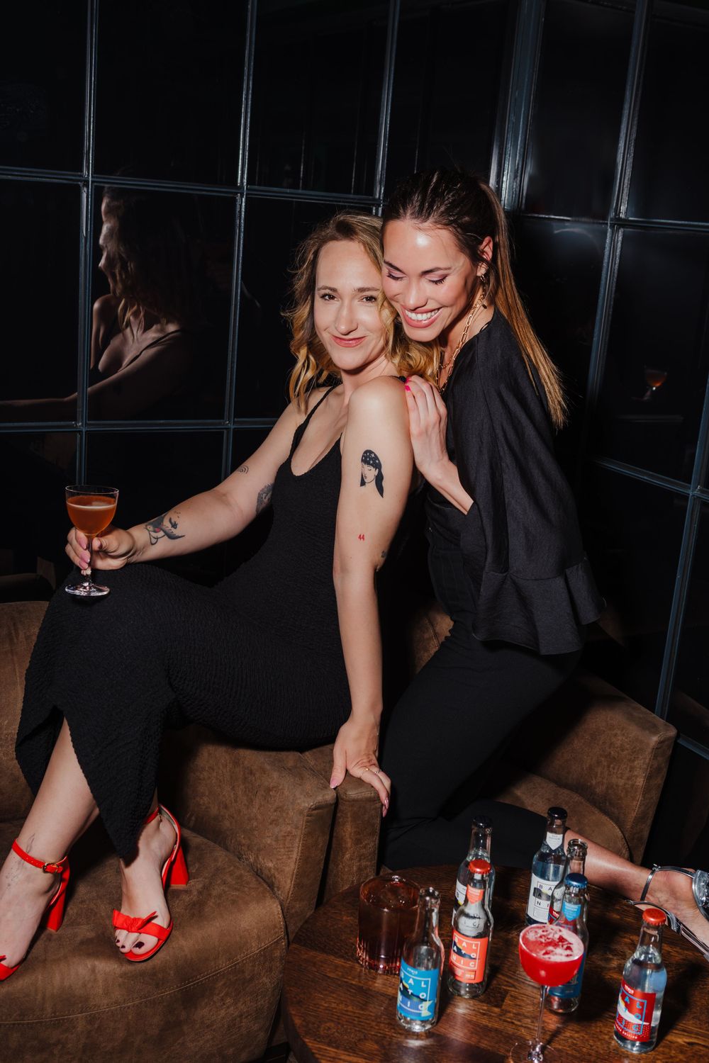 Two people enjoying cocktails and posing playfully on a brown leather couch.