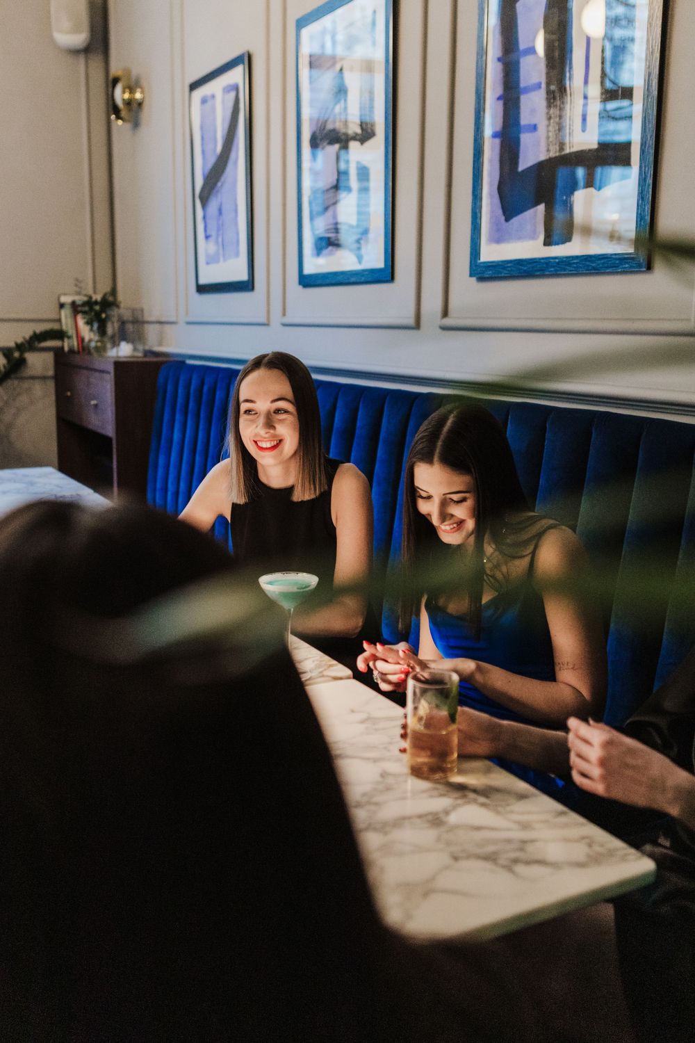 People enjoying drinks at marble table in restaurant with blue nautical artwork.