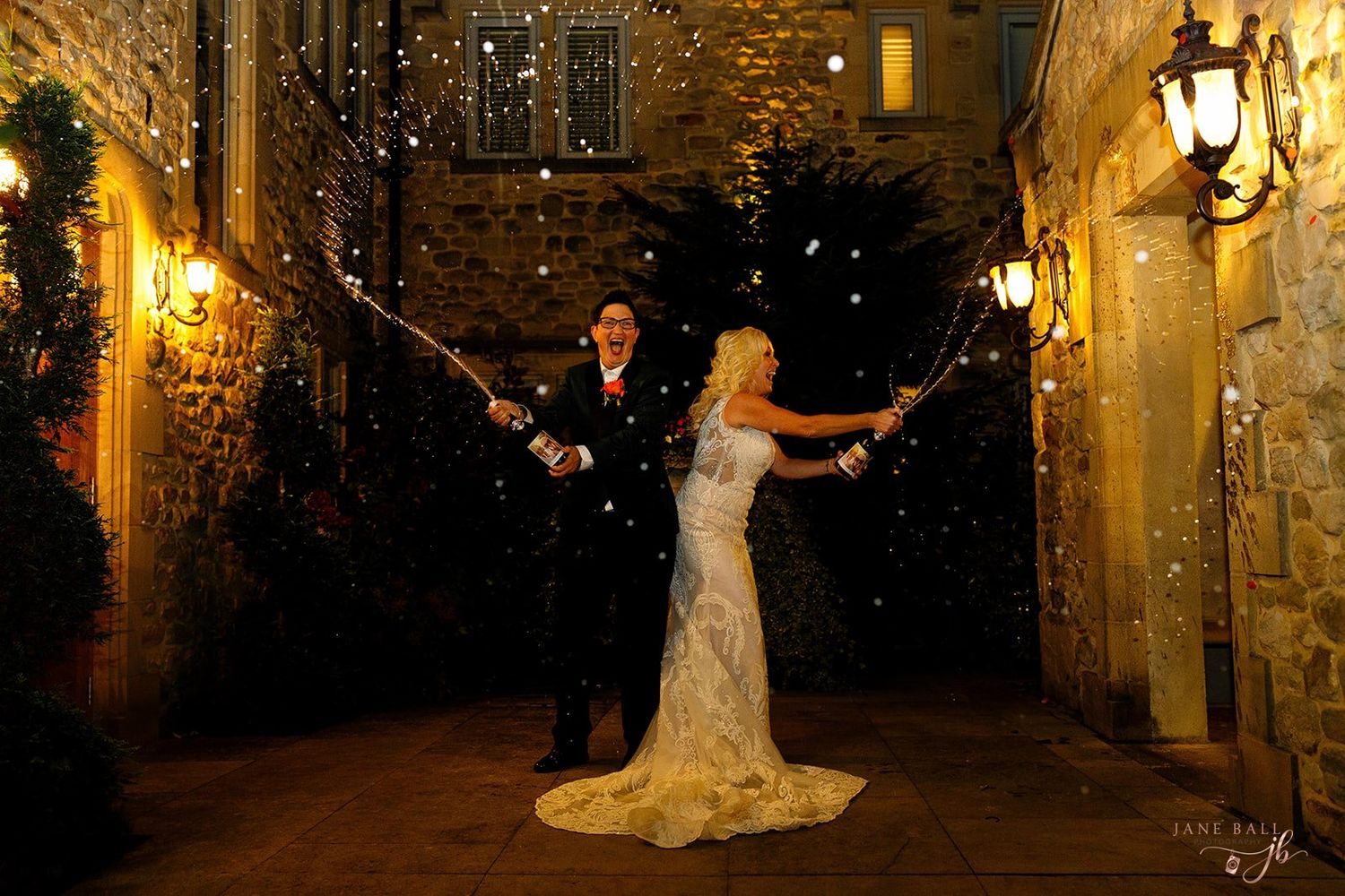 Romantic evening wedding photos of couples in formal attire illuminated by warm glowing lanterns against stone walls.