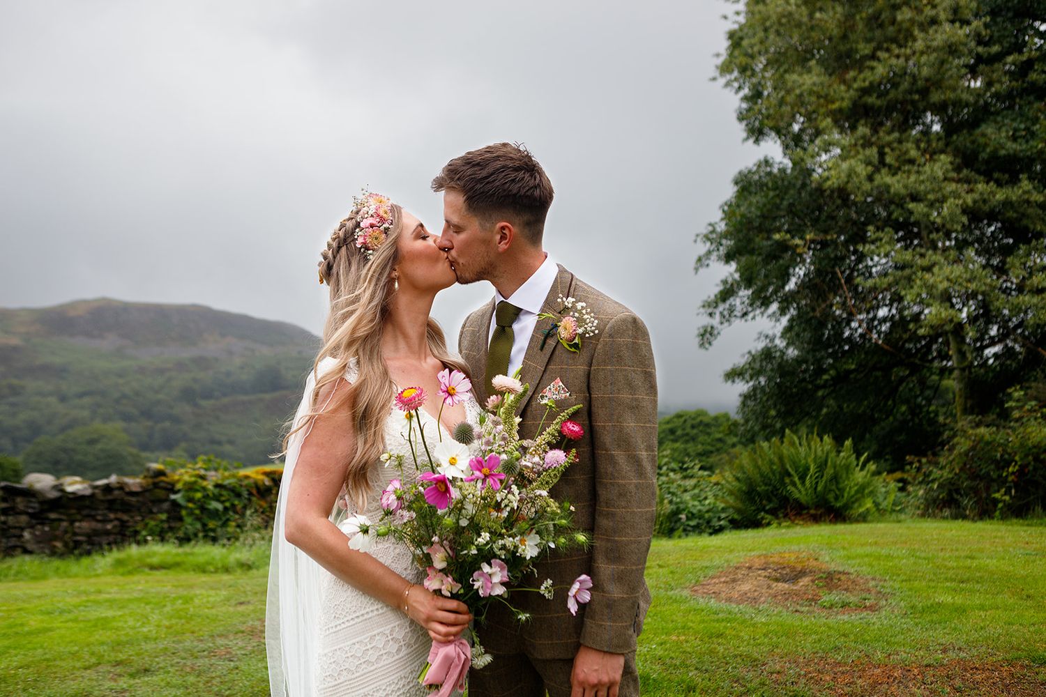 Couple embraces in romantic outdoor setting with rolling hills and lush greenery in background at Fairbank wedding barn