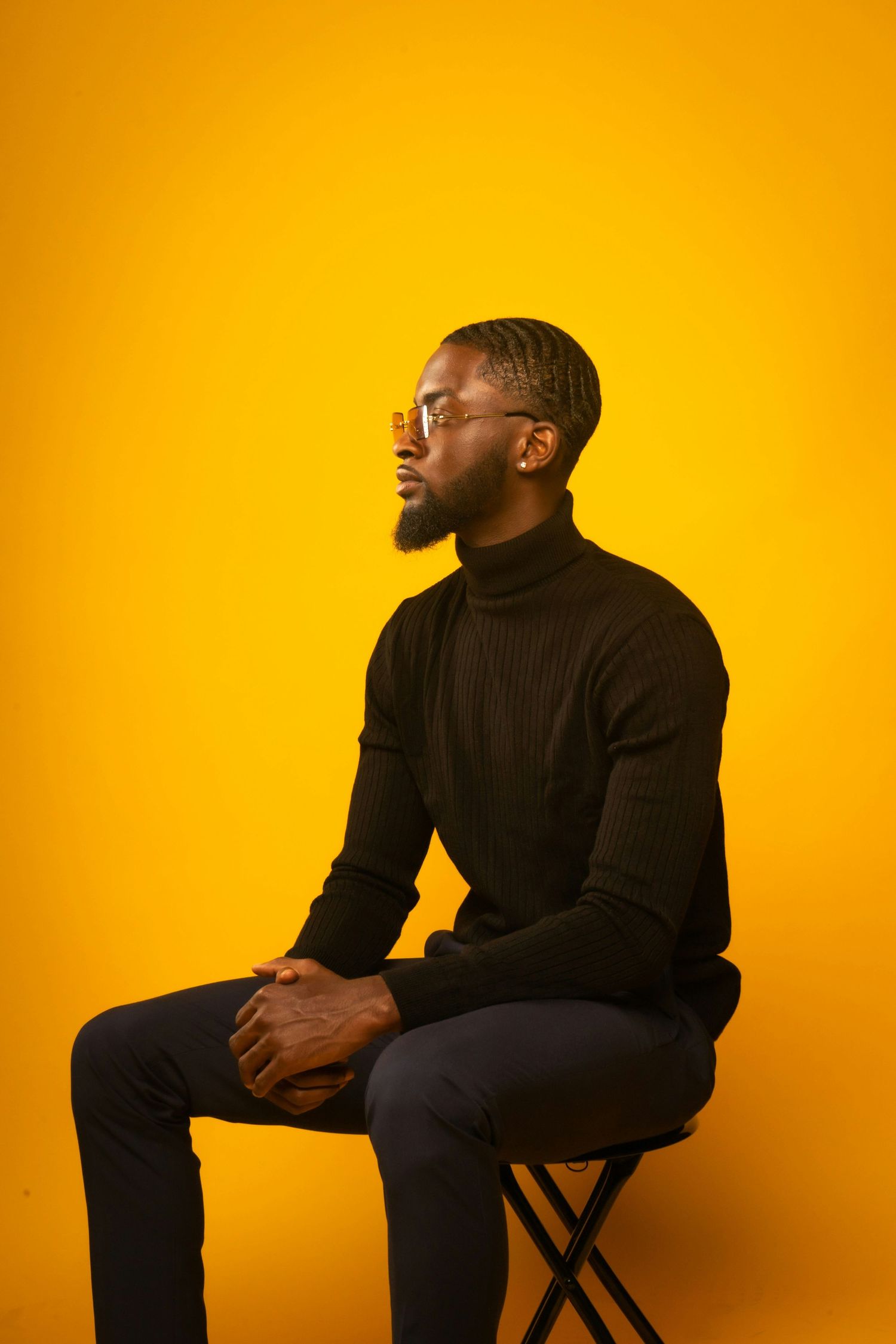 Profile portrait against orange backdrop showing person in black turtleneck seated contemplatively.