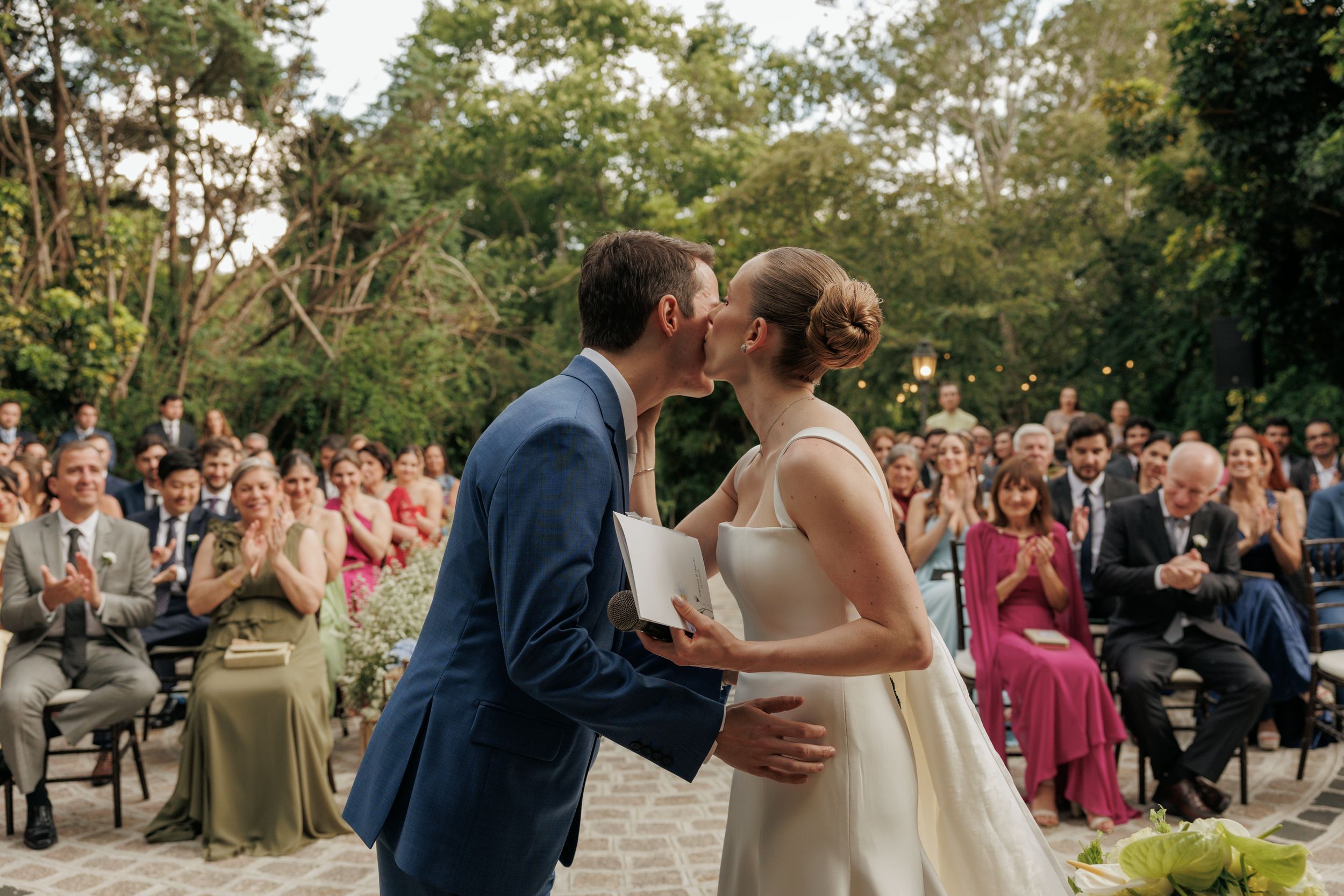 A couple shares romantic moments during their outdoor garden wedding celebration surrounded by guests and natural scenery.