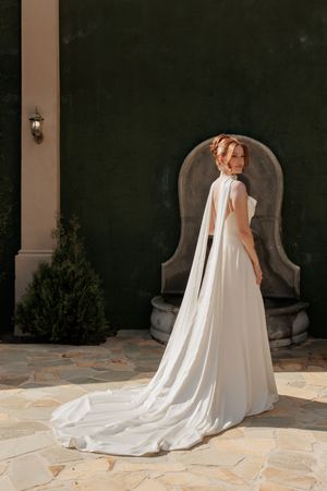 A flowing white bridal cape with a long train cascades across stone pavers in an elegant outdoor setting.