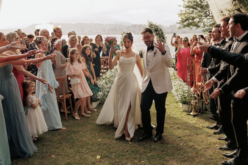 Wedding guests form a joyous walkway on a grassy hillside as newlyweds exit their ceremony.