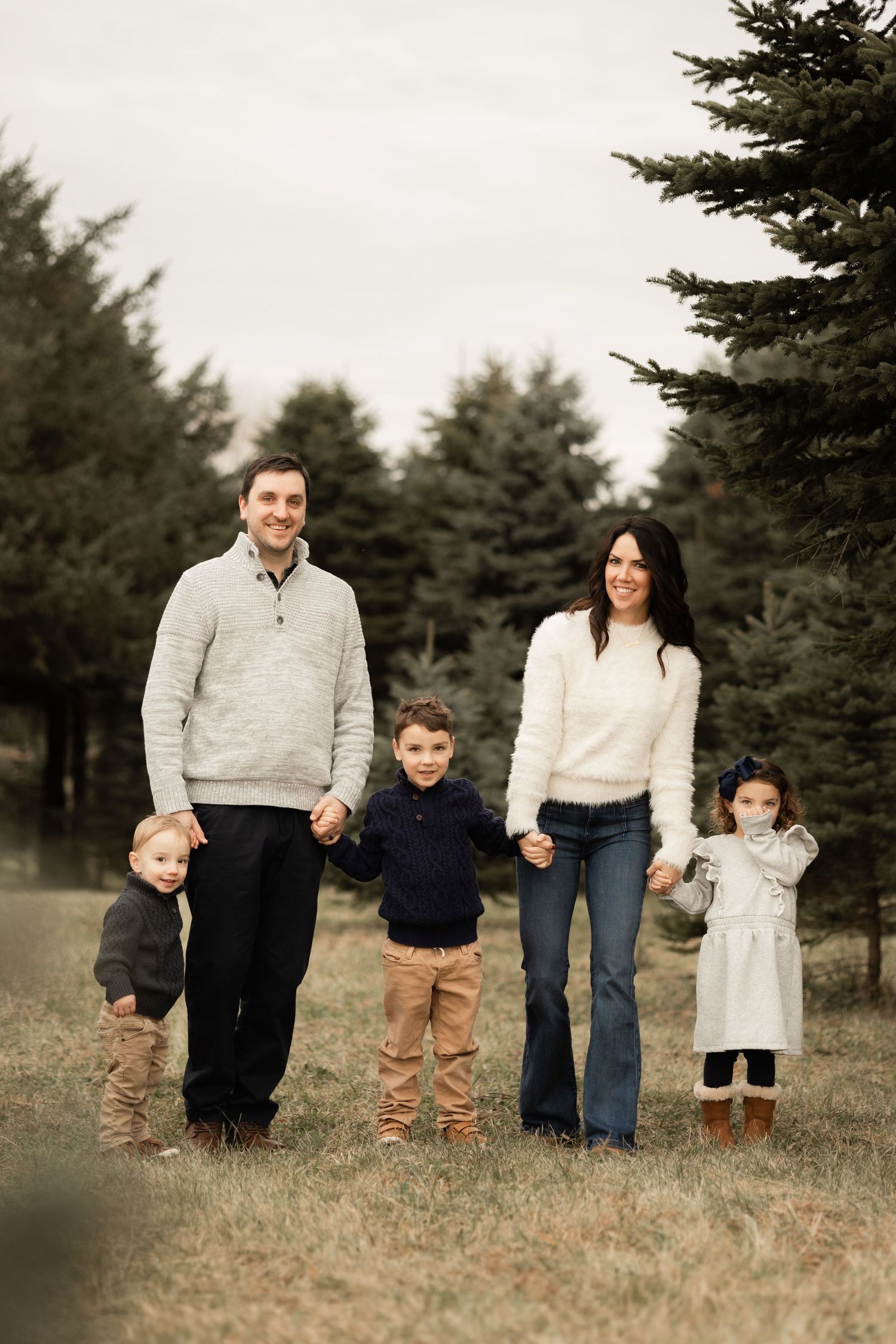Family of five standing together outdoors in winter clothing against evergreen trees in natural setting.