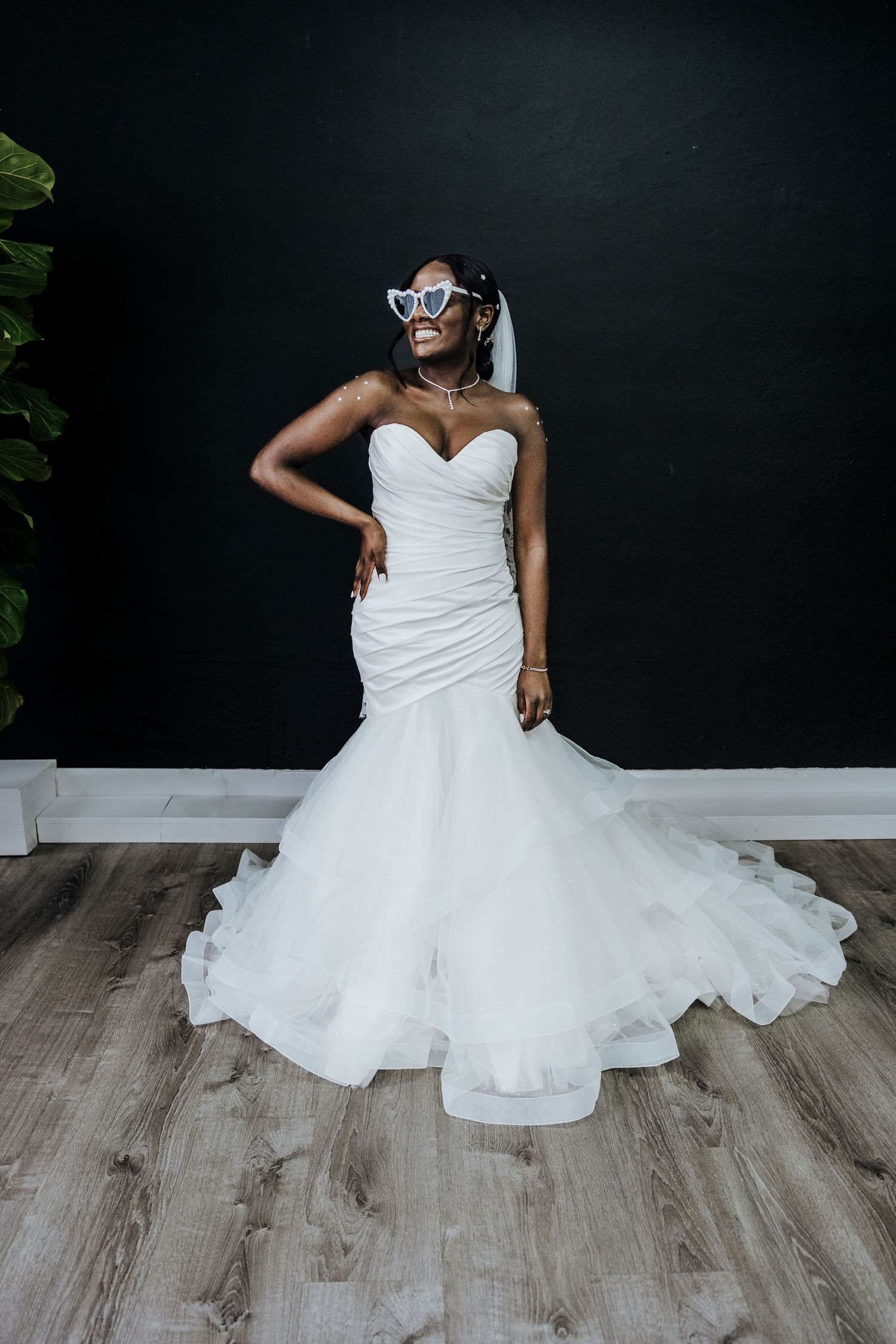 african american Bride poses for the camera with heartshaped glasses in front of a black wall