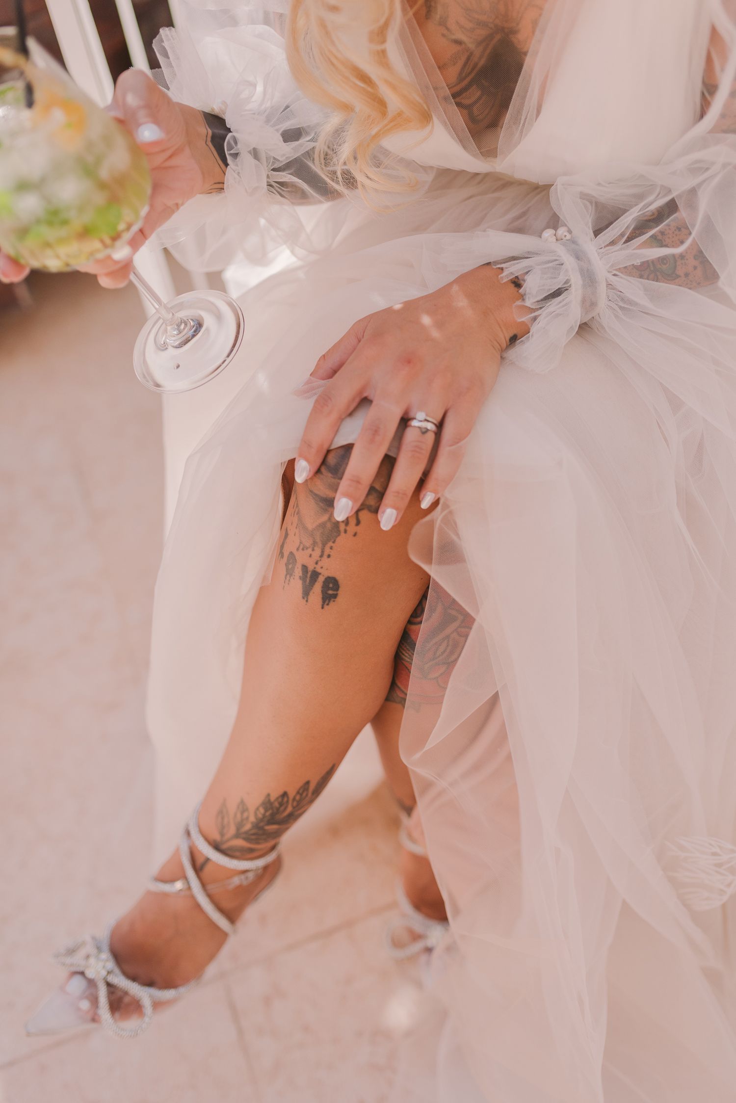 Close-up of bride's tattooed leg and wedding ring while holding champagne glass.