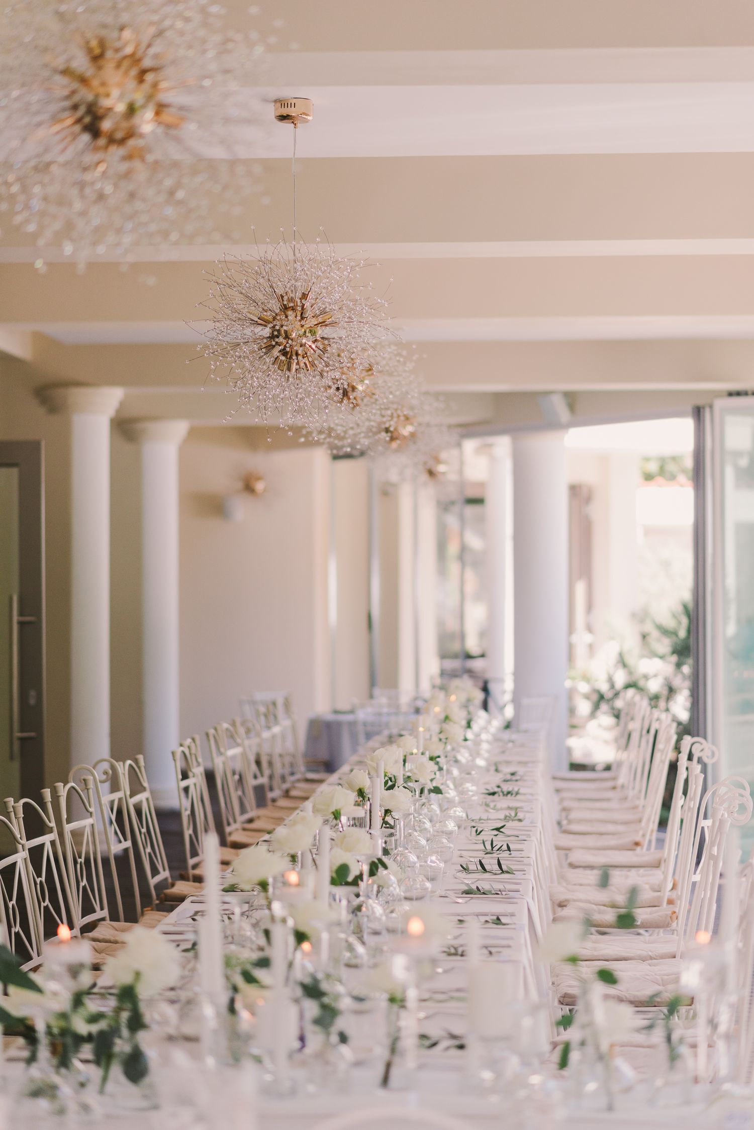 Elegant wedding reception table with white linens and floral centerpieces under crystal chandeliers.