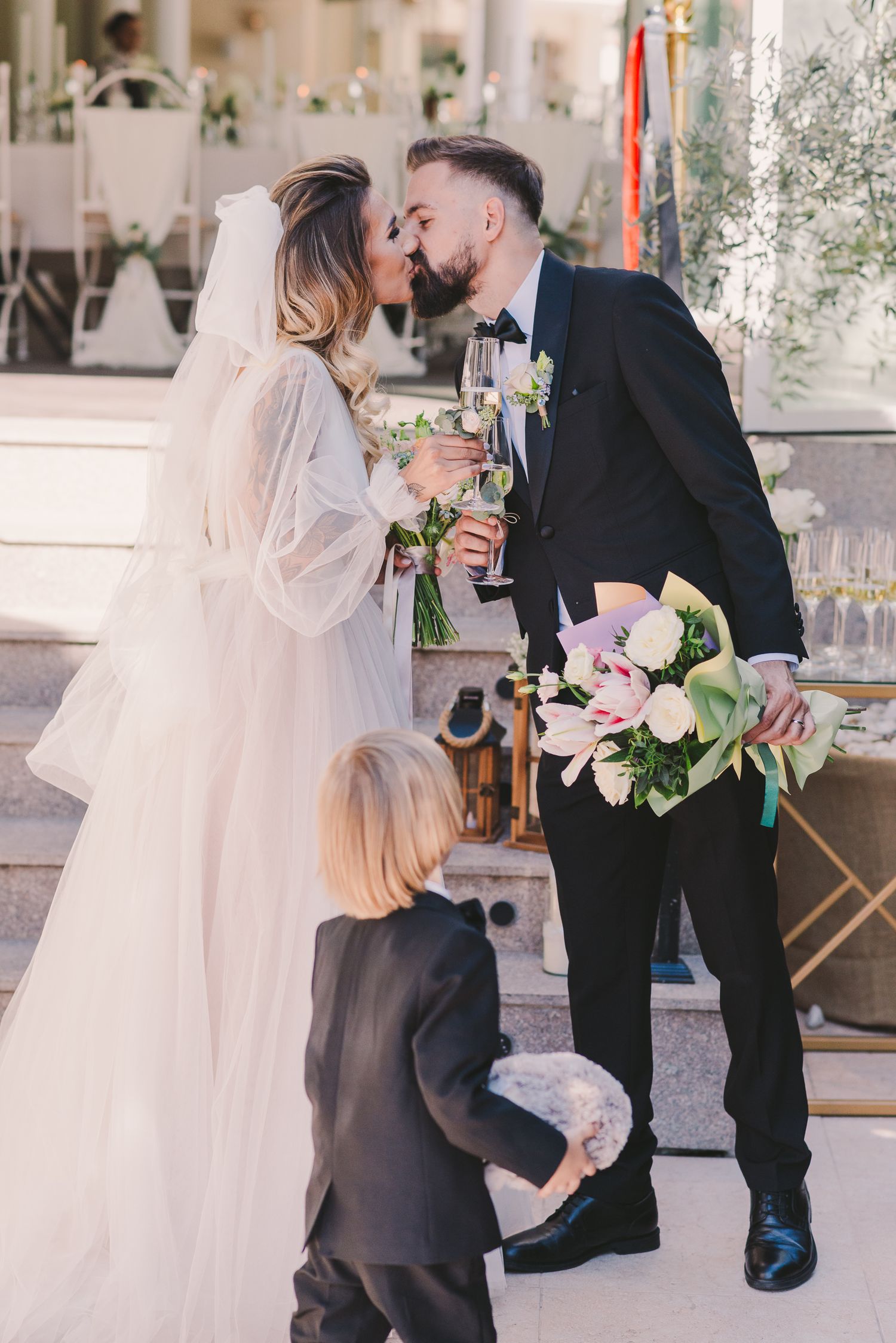 Wedding couple shares intimate moment while young attendant watches at elegant venue.