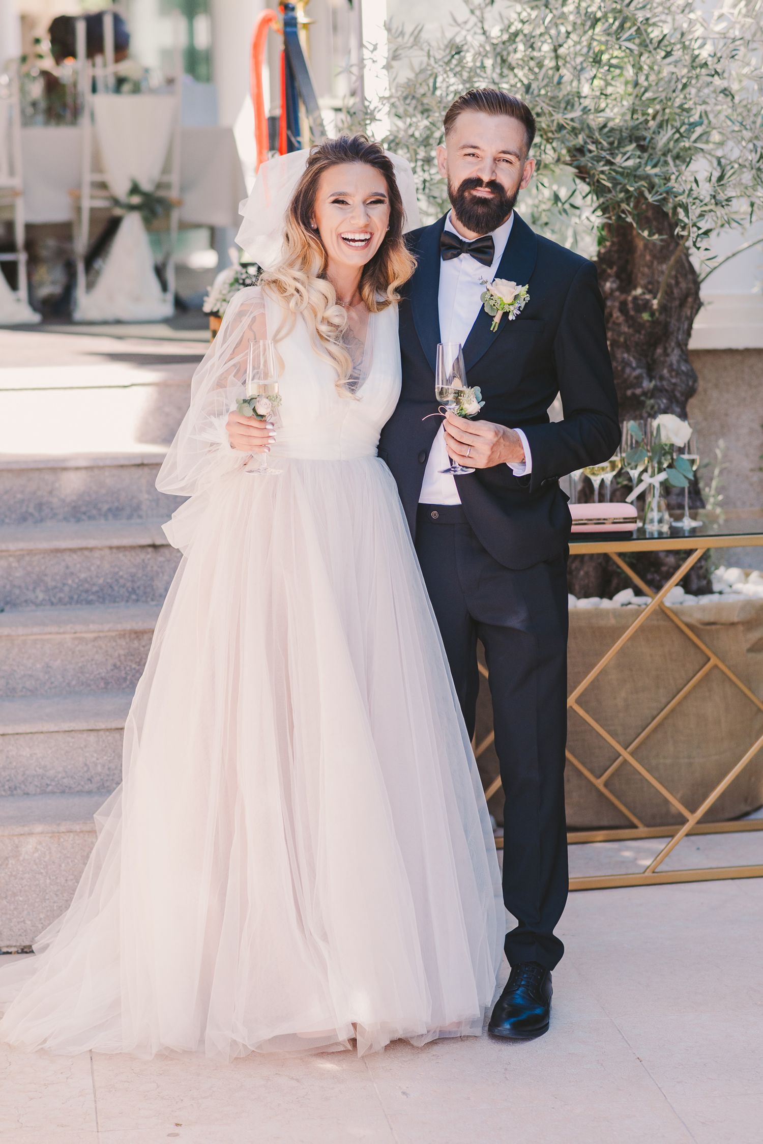 Happy couple in formal wedding attire standing on stone steps.