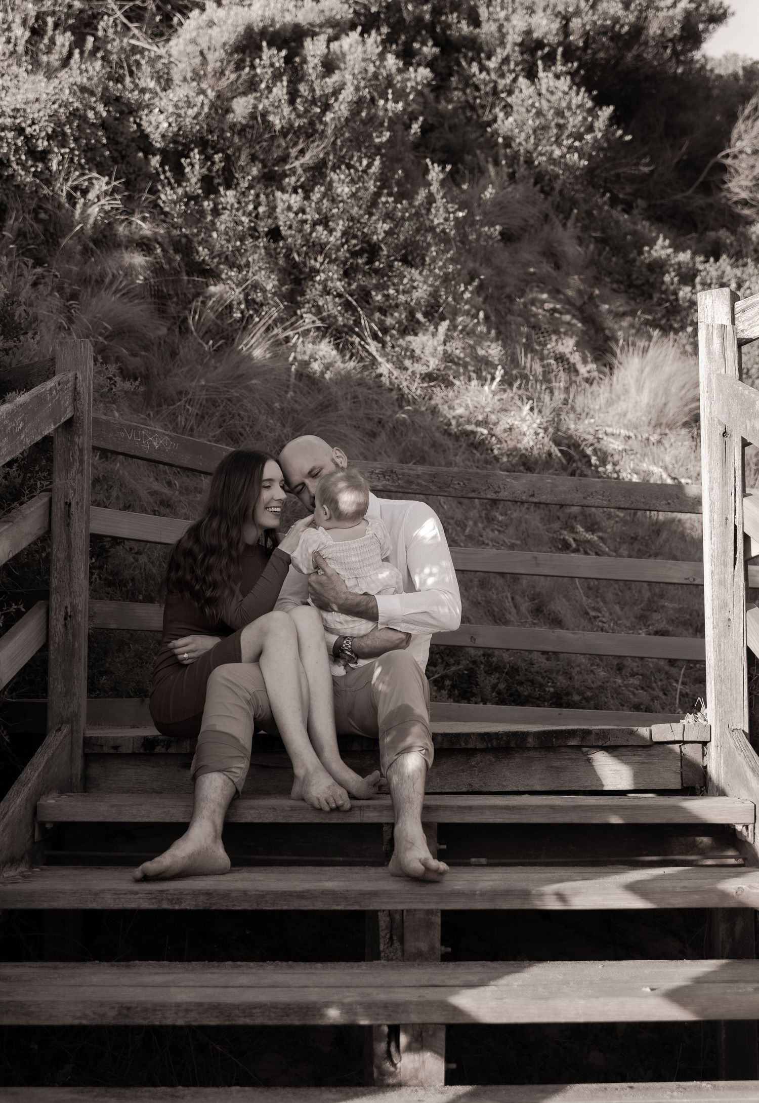 Couple shares intimate moments on a wooden bench in black and white photography.