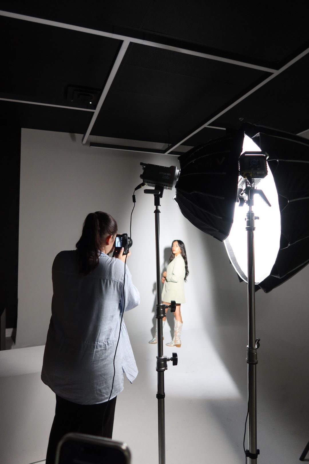 Professional photography studio setup with model posing against white backdrop.