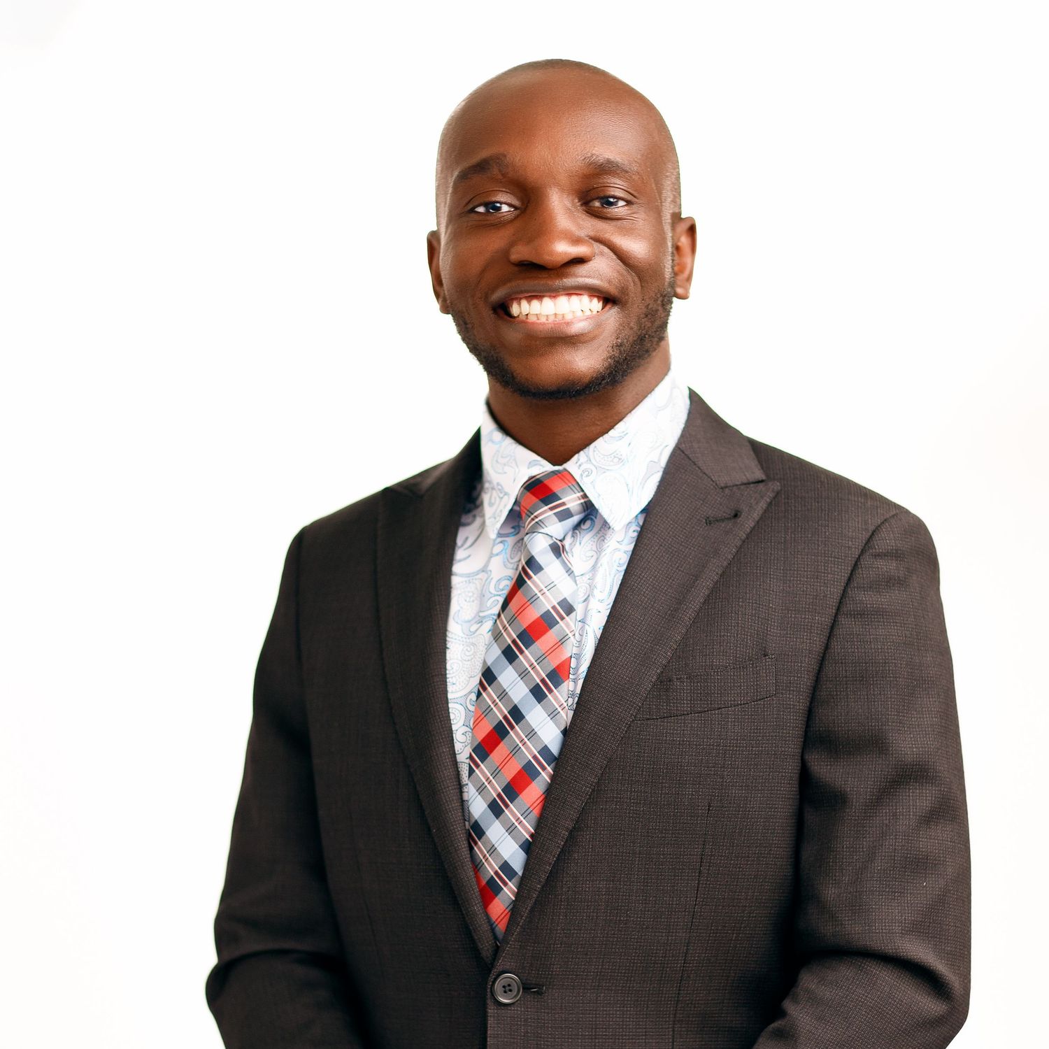 Professional wearing a dark suit and red plaid tie smiles warmly against white background.