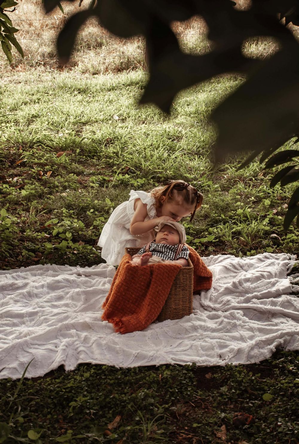 toddler sister and newborn brother connecting/ playing beneath the fruit trees.