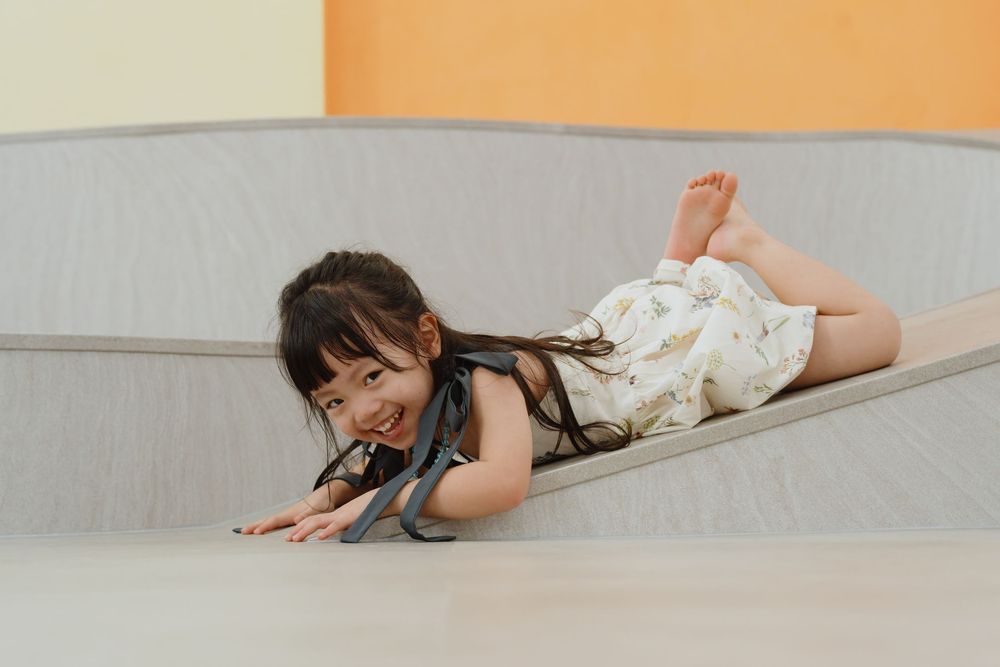 A happy young girl slides down a foam play structure, smiling joyfully in a floral outfit.