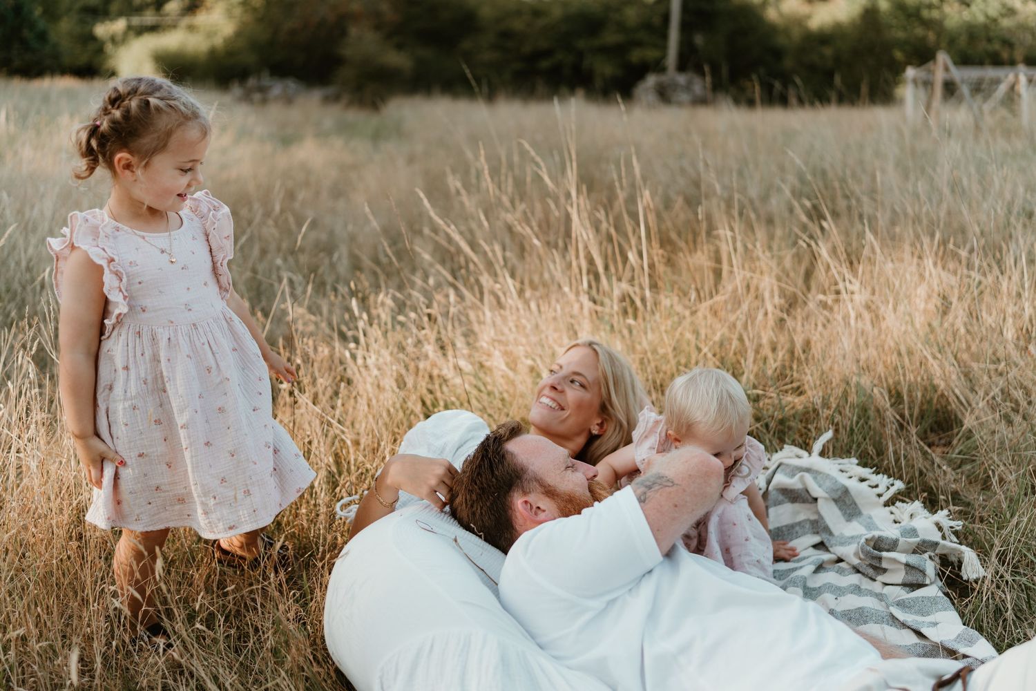 Family relaxing together in tall grass field during golden hour.