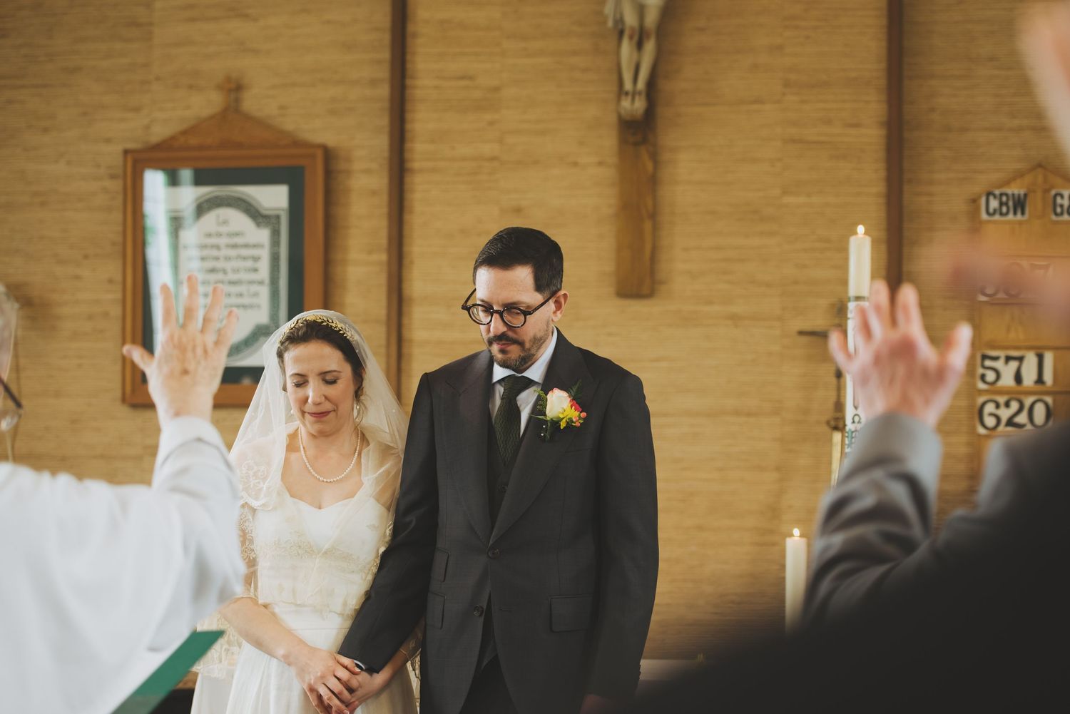 A couple stands together during a church wedding ceremony with raised hands visible from guests in the background.
