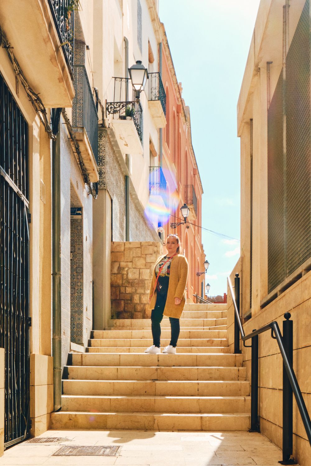 Sunny narrow stone stairway between historic buildings with traditional street lamp.