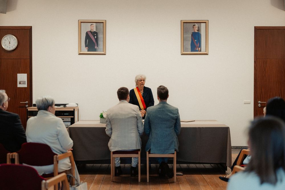 An official ceremony taking place in a simple room with framed portraits on the wall.