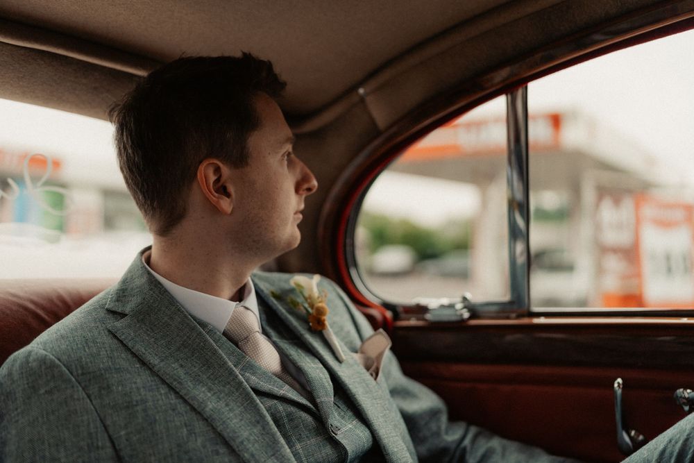 Side profile view of passenger looking out vintage car window in grey suit.