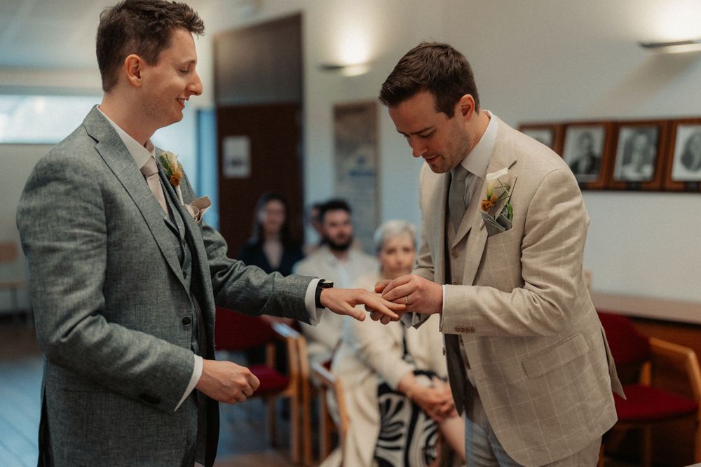 A close-up of two people exchanging rings during an indoor ceremony.