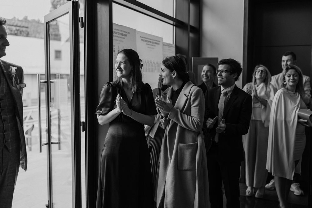 A group of formally dressed guests gathering near a glass entrance door.