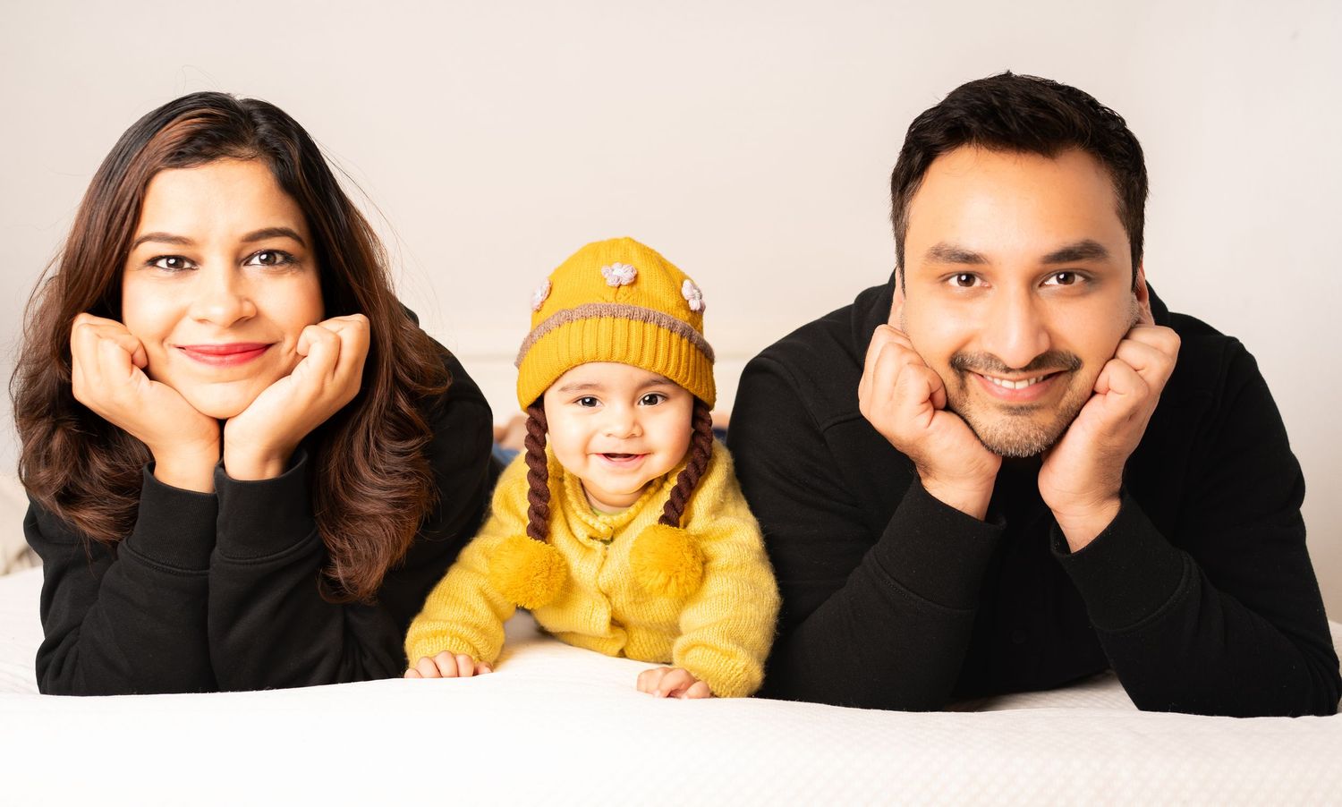 Family portrait with parents and child in yellow beanie against white background.
