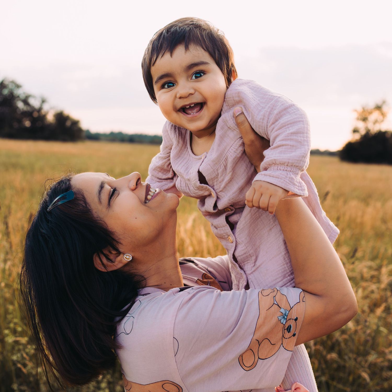Parent and child share joyful moment in golden field during sunset.