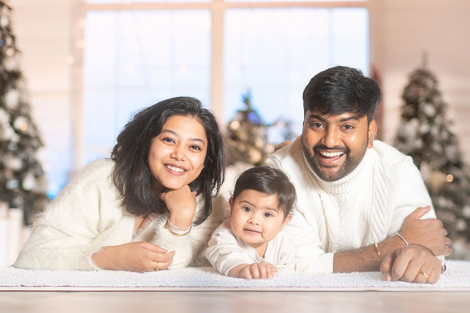 Family wearing white clothes pose together with holiday decorations in background.