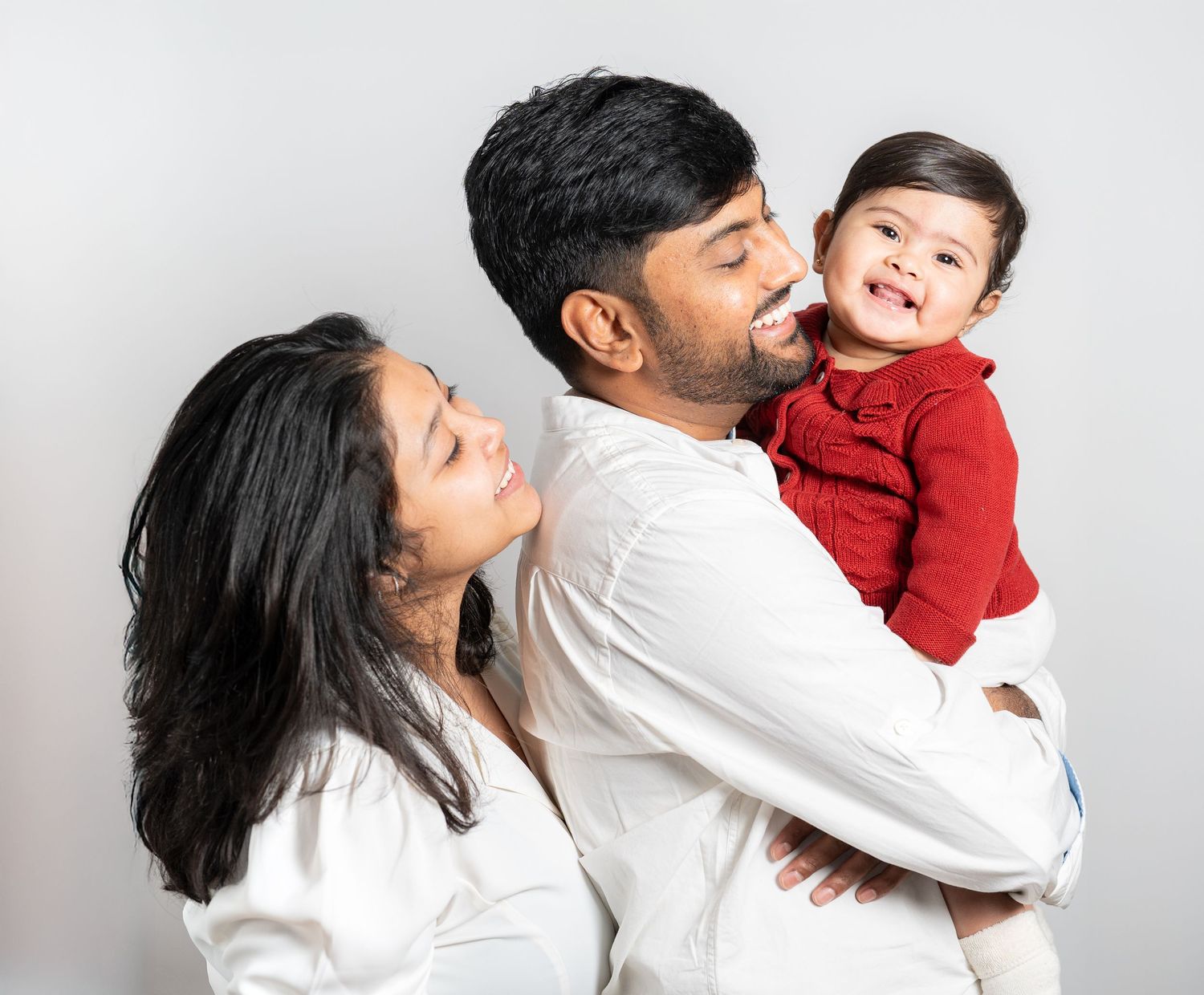 Family shares an intimate moment together while wearing coordinating white outfits against a light background.