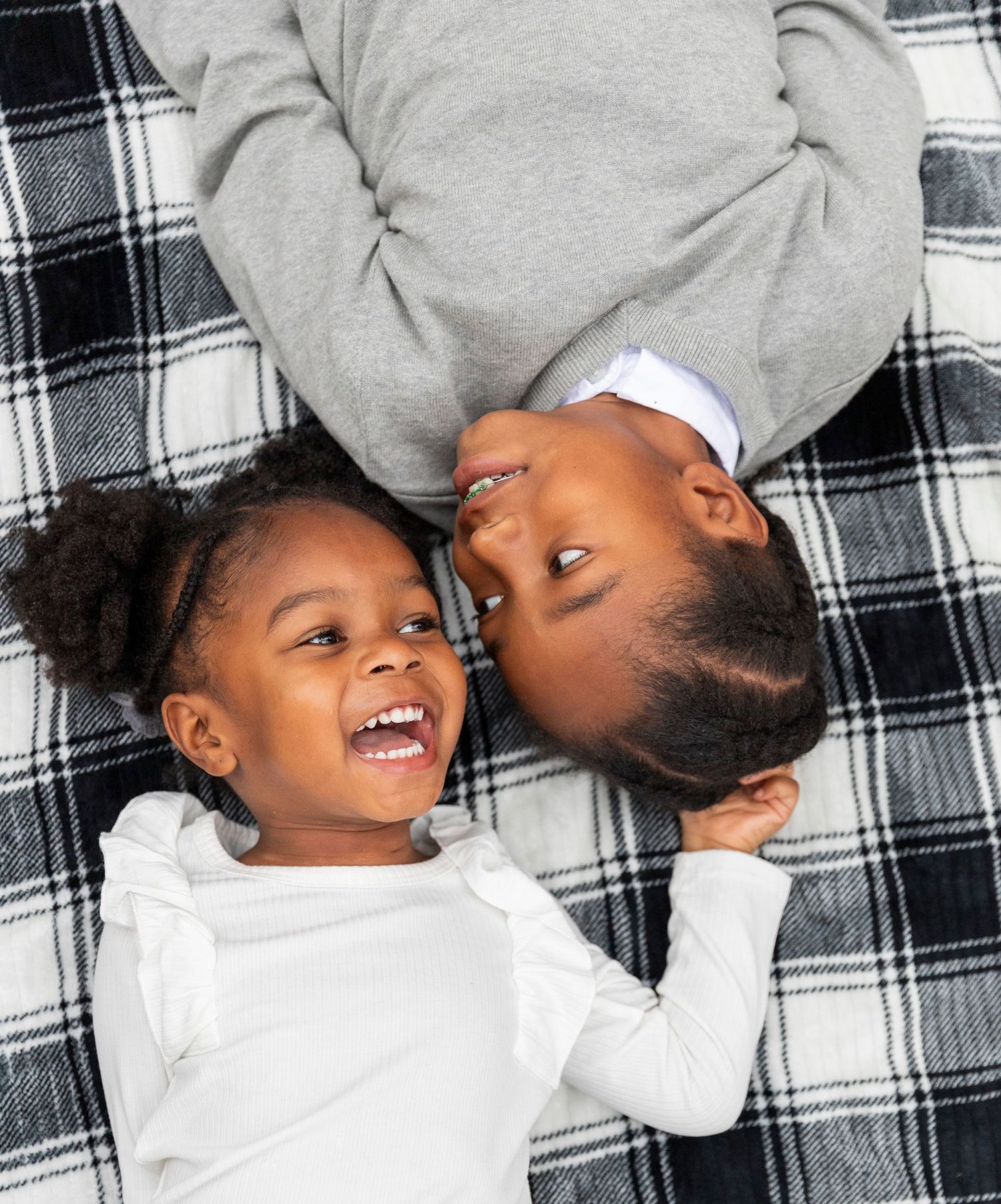 Two children lying on a black and white plaid blanket laughing and smiling together.