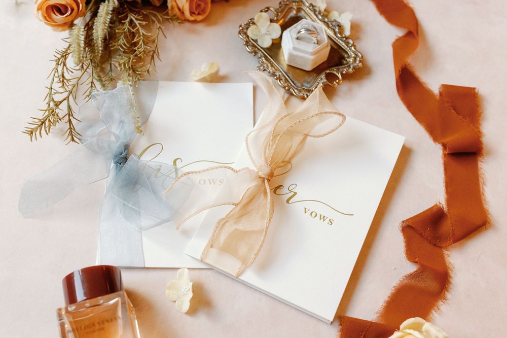Elegant wedding invitation flat lay with dried flowers, rust ribbon, and neutral stationery on white background.