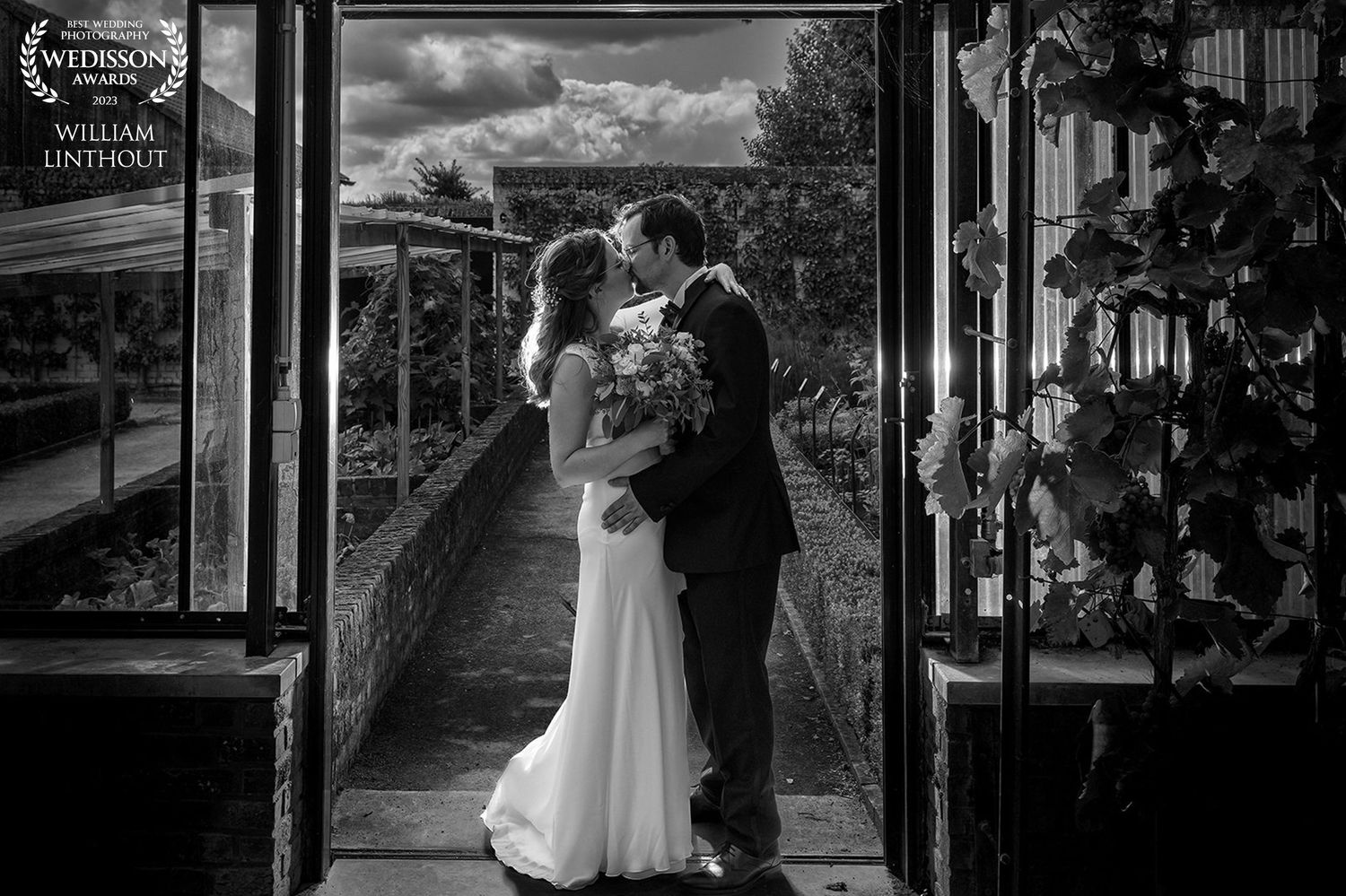 Black and white wedding portrait of couple standing in doorway framed by natural light.