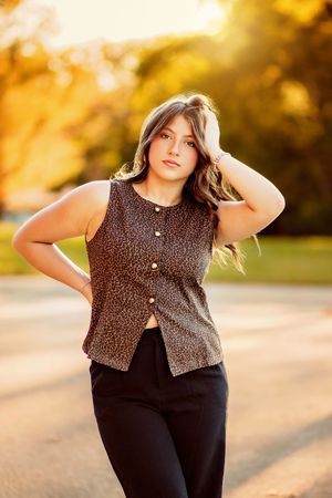Young woman in leopard print vest and black pants posing outdoors during golden hour sunset. Hanover PA Fall Senior Pictures