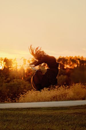 Silhouette of a person jumping joyfully against a warm golden sunset sky with trees in background. Hanover PA Dance Senior Pictures, Dance