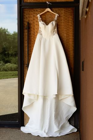 Elegant white A-line wedding dress with lace bodice hanging on wooden door before ceremony.