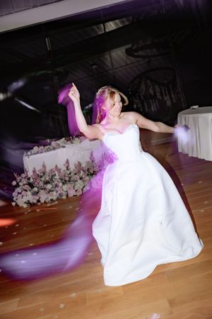 Bride in white strapless gown dances energetically with purple veil swirling on reception dance floor.
