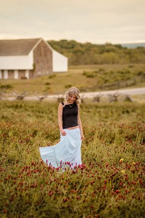 Blonde woman in black top and white skirt twirling in a wildflower field at sunset. Gettysburg Senior Pictures in a field
