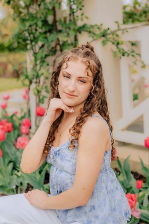 Young woman with curly hair posing thoughtfully near red tulips and white garden pergola. Hershey Gardens Senior Pictures
