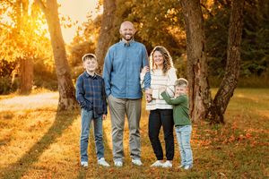 Happy family of four posing together in autumn park with golden foliage at sunset.