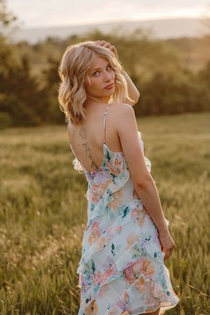 Blonde woman in floral sundress looking over her shoulder in a golden sunlit field. Gettysburg Senior Pictures