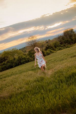 Blonde woman in floral dress running through a green field at golden hour sunset. Gettysburg Senior Pictures
