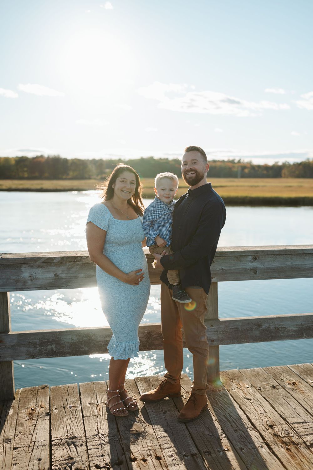A family stands together on a wooden dock overlooking a serene waterfront on a sunny afternoon.