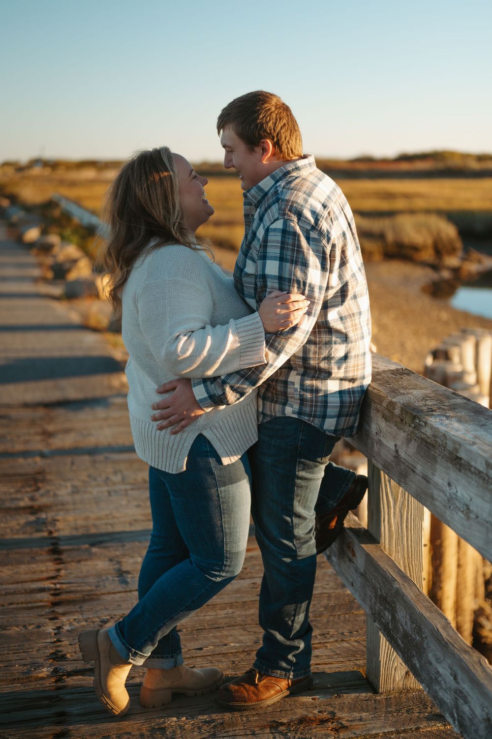 Two children play and interact on a wooden boardwalk at sunset with golden light illuminating the coastal landscape.